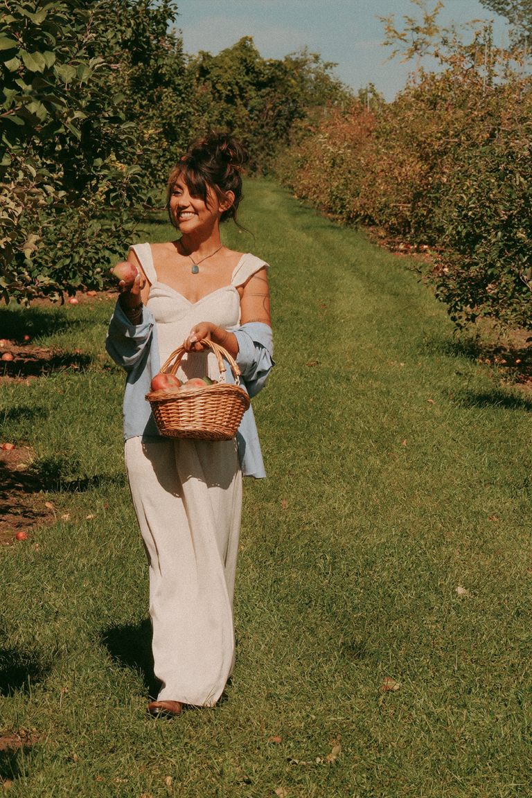 Woman walking through an apple orchard with an apple during a seasonal photography session in Ottawa