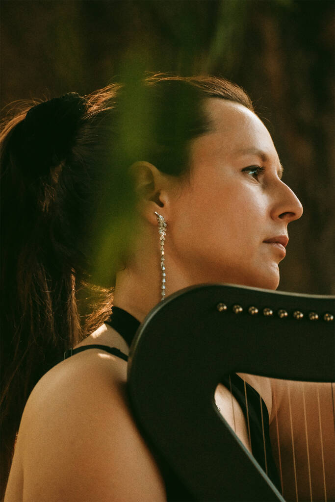 An electric harp player performing outdoors under a weeping willow tree by a pond in Ottawa